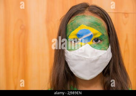 Enfant avec un masque avec son visage peint avec le drapeau du Brésil. Banque D'Images