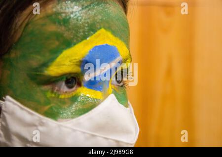 Enfant avec un masque avec son visage peint avec le drapeau du Brésil. Banque D'Images