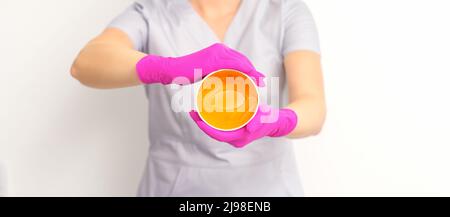 Portrait d'une esthéticienne caucasienne tenant un pot de pâte de sucre pour sugarer portant des gants roses sur fond blanc Banque D'Images