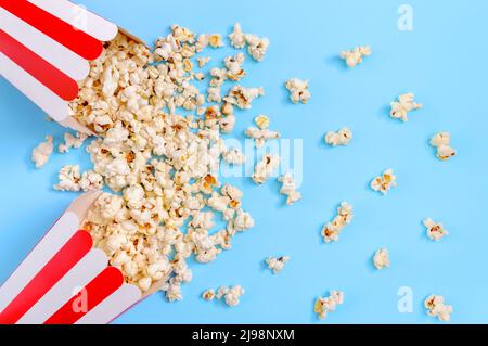 Le pop-corn sort des gobelets en papier à rayures sur un fond bleu, vu d'en haut. Cinéma, cinéma et divertissement Banque D'Images