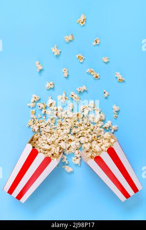 Le pop-corn sort des gobelets en papier à rayures sur un fond bleu. Un peu de pop-corn. Vue verticale. Banque D'Images