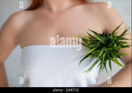 Gros plan. Rogné. Une femme dans une serviette blanche tient une aisselle dans un pot avec une plante simulant une végétation indésirable sur son corps. Épilation. Épilation Banque D'Images