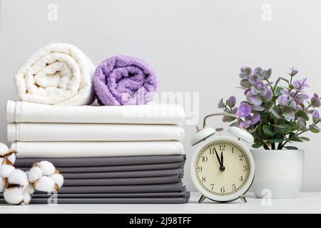 Pile de linge de lit, draps et serviettes avec branche en coton et réveil en pot sur table Banque D'Images