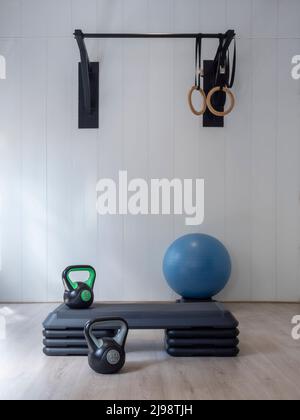 Chambre sans personnes avec des anneaux et un bar dans une salle de gym. Kettlebells à côté d'un banc. Fond blanc et parquet. Un mode de vie sain Banque D'Images