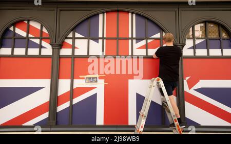 Un homme décorant des fenêtres de magasin avec un drapeau Union Jack pour les célébrations du Jubilé de platine de la reine Elizabeth. Banque D'Images