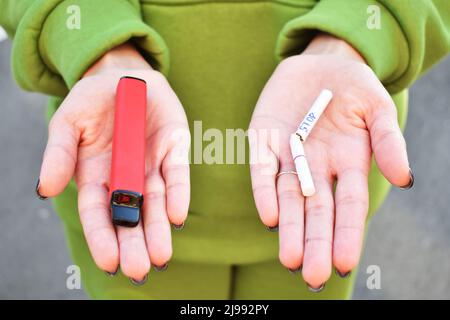 Vue rapprochée des mains de femmes tenant une cigarette électronique dans une main et une cigarette à la nicotine dans une autre. Concept de choix. Banque D'Images