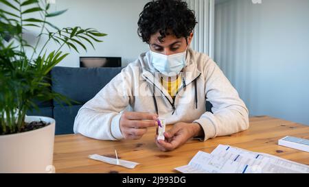 Un homme portant un masque plaçant l'échantillon dans le dispositif de test diagnostique de l'antigène covid-19 à la maison. Kit de cassette pour auto-test pour vérifier l'entrée Banque D'Images