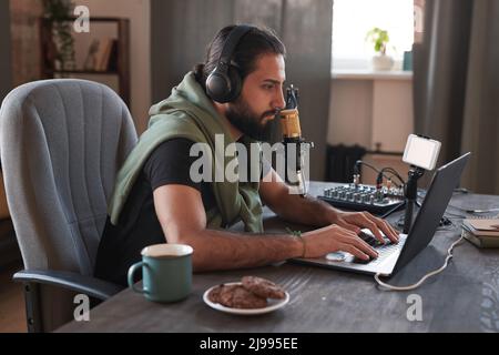 Portrait horizontal à vue latérale moyenne d'un homme d'influence moderne du Moyen-Orient assis devant un ordinateur portable lisant les commentaires Banque D'Images