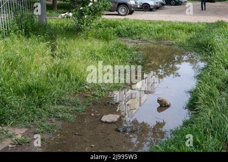 Égout de percée d'eau. Percée d'eau dans la conduite de chauffage, l'eau coule sous le couvercle d'égout sur la route Banque D'Images