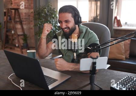 Portrait horizontal moyen de joyeux moderne barbu jeune homme moyen-oriental gagnant jeu pendant le flux en ligne Banque D'Images