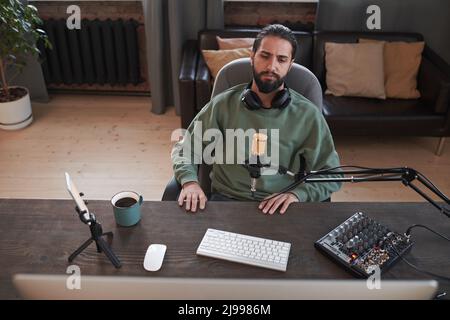Portrait horizontal haut angle moyen de jeune moderne moyen-oriental blogueur assis à un bureau regardant quelque chose pour la vidéo de réaction Banque D'Images