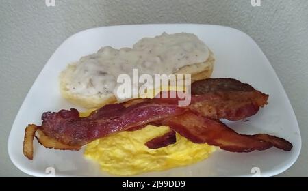 Un petit-déjeuner américain traditionnel composé de tranches de bacon tremblantes, d'une patty de saucisse de porc, d'œufs brouillés et d'un petit-déjeuner avec sauce à la saucisse de style campagnard de Windy Hollow Biscuit House est conçu pour une photo posée le dimanche 8 mai 2022 à Owensboro, comté de Daviess, KY, ÉTATS-UNIS. Windy Hollow Biscuit House est un nouveau restaurant appartenant à la même famille que le Windy Hollow Restaurant original, qui reste ouvert dans la campagne du comté de Daviess. (Photo APEX MediaWire par Billy Suratt) Banque D'Images