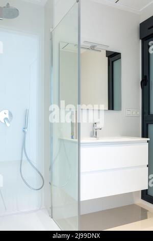 Partie d'une salle de bains moderne. Vue sur une cabine de douche en verre et une armoire avec lavabo. Banque D'Images