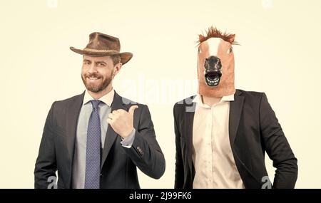 Homme heureux point doigt à l'homme d'affaires étrange portant le masque de tête de cheval dans les vêtements de formalwear, partie occidentale Banque D'Images