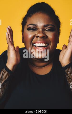 gros plan portrait d'une jeune femme noire adulte en riant avec la bouche ouvert sourire toothy sur fond jaune studio Banque D'Images