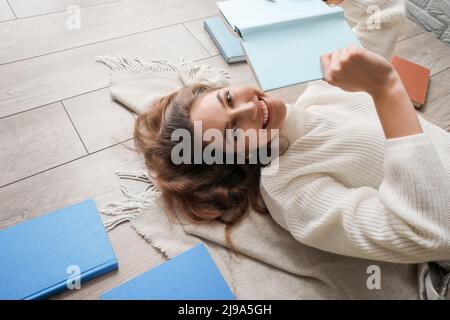 Belle femme souriante couchée sur un parquet avec un livre Banque D'Images