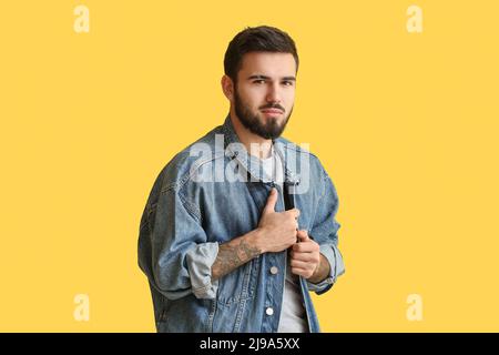 Jeune homme à barbe portant une veste en denim sur fond jaune Banque D'Images