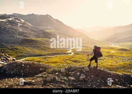 Silhouette de l'homme Hiker touriste homme avec grand sac à dos debout sur la roche contre beau coucher de soleil et rivière dans la vallée de la montagne. En plein air et en randonnée Banque D'Images
