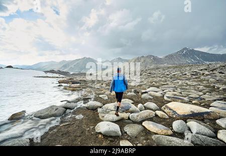 Homme avec en blouson bleu marchant sur la vallée rocheuse dans les belles montagnes contre ciel nuageux Banque D'Images