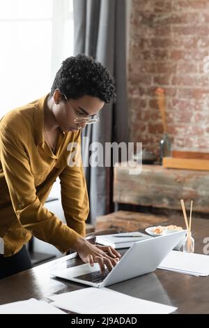 Une femme africaine attentionnés se penche sur le bureau et travaille sur un ordinateur portable Banque D'Images