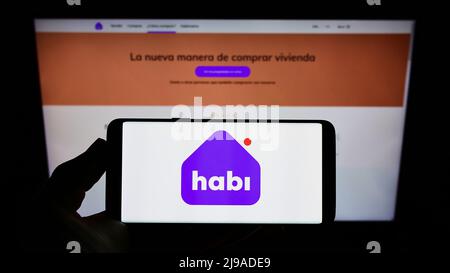 Personne tenant le téléphone portable avec le logo de la société colombienne INVERSIONES MCN S.A.S (Habi) sur l'écran en face de la page web. Mise au point sur l'affichage du téléphone. Banque D'Images