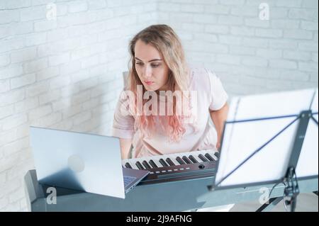 Une femme amicale joue le piano électronique et dirige un blog vidéo sur son ordinateur portable. Restez à la maison. Professeur d'instruments de musique. Musique d'apprentissage à distance Banque D'Images