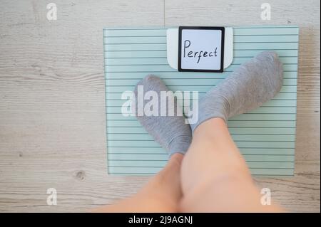 Une femme sans visage mesure le poids sur les balances de sol. Vue de dessus des pieds pour femmes en chaussettes grises sur la balance avec le mot Perfect. L'inscription sur le Banque D'Images