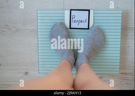 Une femme sans visage mesure le poids sur les balances de sol. Vue de dessus des pieds pour femmes en chaussettes grises sur la balance avec le mot Perfect. L'inscription sur le Banque D'Images