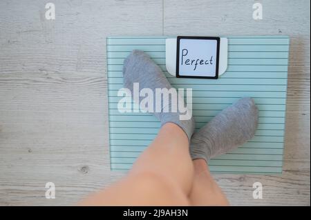 Une femme sans visage mesure le poids sur les balances de sol. Vue de dessus des pieds pour femmes en chaussettes grises sur la balance avec le mot Perfect. L'inscription sur le Banque D'Images