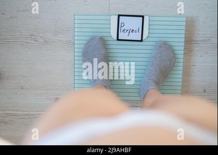 Une femme sans visage mesure le poids sur les balances de sol. Vue de dessus des pieds pour femmes en chaussettes grises sur la balance avec le mot Perfect. L'inscription sur le Banque D'Images