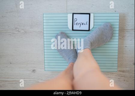 Une femme sans visage mesure le poids sur les balances de sol. Vue de dessus des pieds pour femmes en chaussettes grises sur la balance avec le mot Perfect. L'inscription sur le Banque D'Images