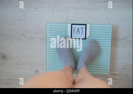 La femme mesure son poids. Une vue de dessus des pieds femelles en chaussettes grises se trouve sur une échelle électronique. L'inscription FAT sur l'affichage du sol Banque D'Images