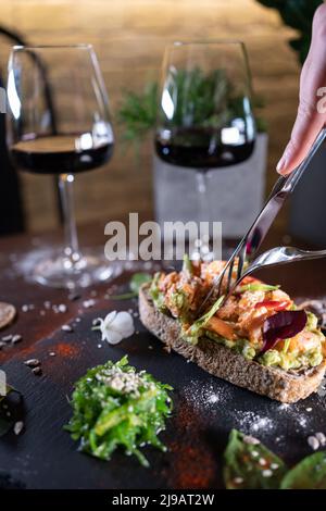 la personne mange un sandwich frais avec de l'avocat, du poisson frit au saumon rouge, des algues et du vin Banque D'Images