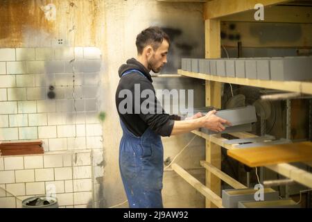 L'employé met la boîte sur une étagère. Homme replie les planches peintes. Guy travaille dans un atelier de bois. Banque D'Images