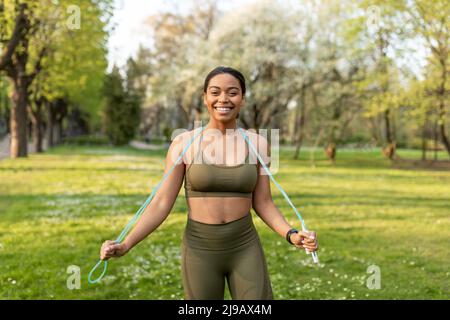 Bonne jeune femme noire dans les vêtements de sport posant avec corde de saut au parc de la ville Banque D'Images