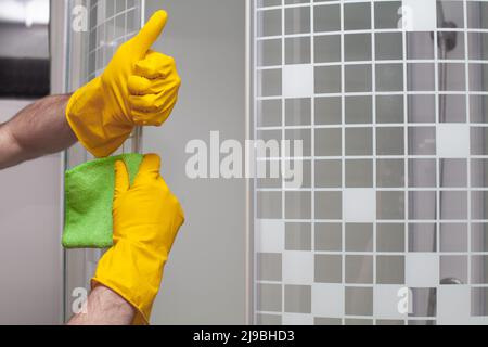 Homme nettoyant la porte en verre dans la salle de bains et montrant le pouce de près Banque D'Images