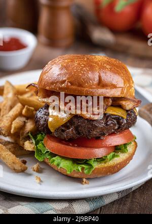 Bacon cheeseburger avec laitue et tomate sur un petit pain grillé et frites sur une assiette Banque D'Images