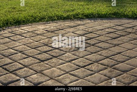 Pavés en béton estampé pavés de pavés, aspect décoratif pavés pavés pavés de pavés de tuiles sur le sol en ciment dans un parc avec pelouse verte Banque D'Images