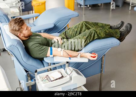 Portrait complet du jeune soldat qui donne du sang en étant allongé sur une chaise confortable au centre du médicament Banque D'Images