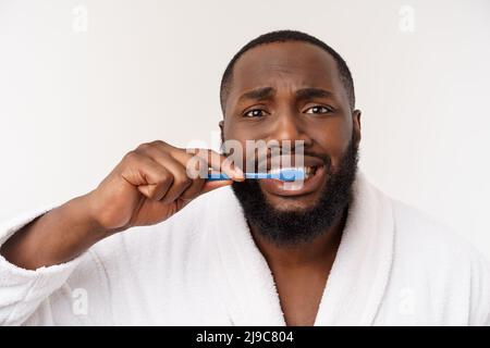 portrait d'un heureux jeune anm foncé se brossant les dents avec du dentifrice noir sur fond blanc. Banque D'Images