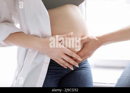 Photo rognée d'un couple enceinte à la maison, l'homme est embrassant et touchant la femme grand ventre. Grossesse, parentalité, amour, concept de famille. Photo de haute qualité. Banque D'Images