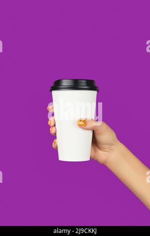 Les femmes ont les mains avec une manucure orange tendance tenant une tasse en papier sur fond violet Banque D'Images