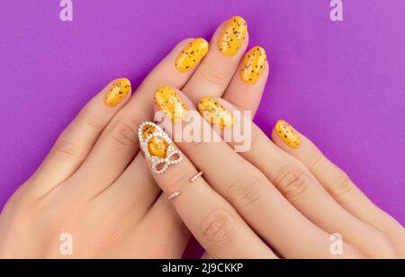 Des mains de femmes soignées avec un motif à ongles tendance sur fond violet Banque D'Images