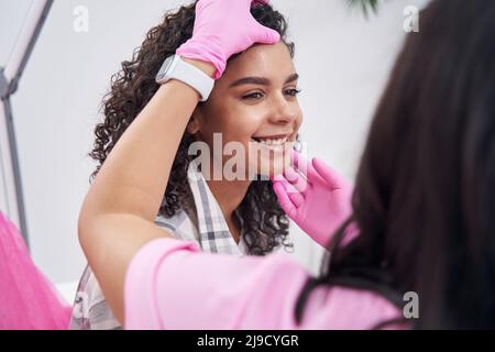 Le médecin touche le visage de la femme avec les deux mains dans des gants roses Banque D'Images