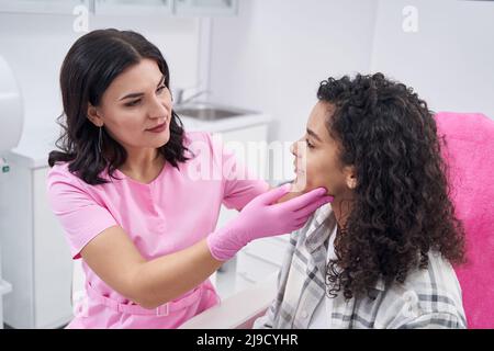 Le médecin avec les mains effectue un examen médical du visage de la femme Banque D'Images