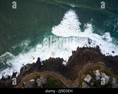 Vue de dessus. Petites maisons sur la côte rocheuse verte de l'océan. Eaux turquoise de l'océan et vagues de mousse blanche. Belle nature, écologique Banque D'Images