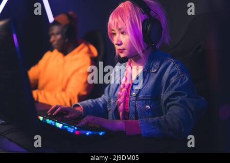 Jeune femme asiatique dans le casque et perruque rose joue des jeux vidéo, homme afro-américain sur le fond de copie espace concept . Photo de haute qualité Banque D'Images