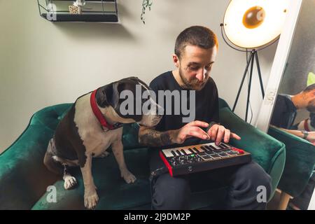 Un créateur caucasien d'âge moyen assis sur un canapé avec son grand chien en utilisant un mélangeur de carte de contrôleur dans son appartement moderne. Photo de haute qualité Banque D'Images