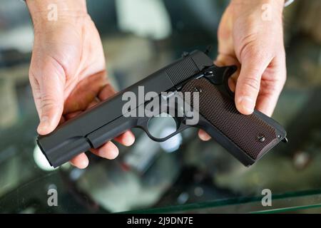 L'assistant d'atelier de gunsmith présente un pistolet noir en mains Banque D'Images