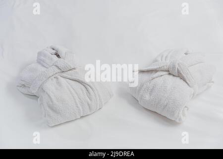 Deux élégants peignoirs blancs pliés sont disposés sur du linge de lit blanc. Personne. Le concept de bon sommeil et de détente, l'hospitalité, le spa et l'auto-soin. Banque D'Images